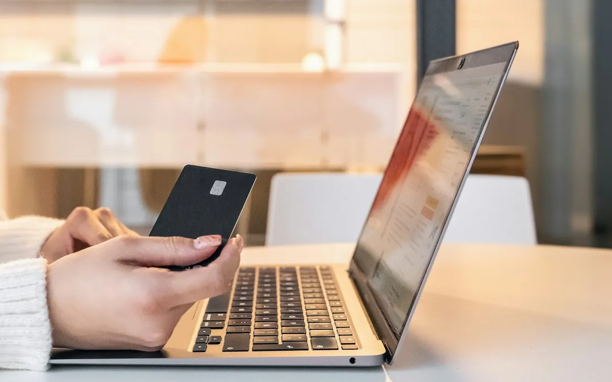 Hands holding a payment card beside an open laptop.